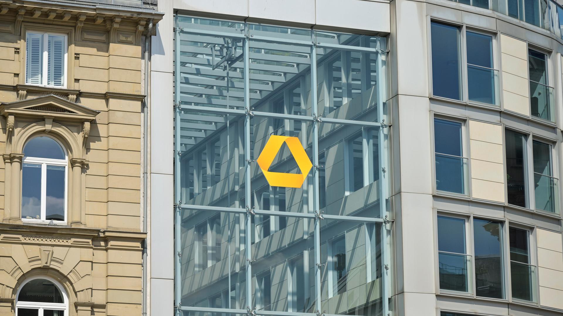 Das gelbe Logo der Commerzbank auf einer Glassfassade in Frankfurt. Links daneben ein Altbau. Das gelbe Logo der Commerzbank auf einer Glassfassade in Frankfurt. Links daneben ein Altbau.