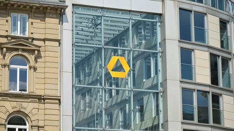 Das gelbe Logo der Commerzbank auf einer Glassfassade in Frankfurt. Links daneben ein Altbau.
