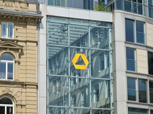 Das gelbe Logo der Commerzbank auf einer Glassfassade in Frankfurt. Links daneben ein Altbau.