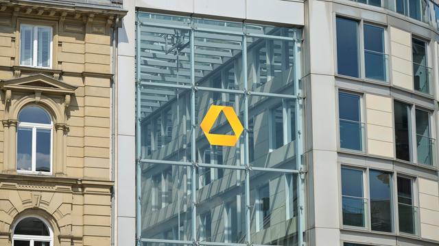 Das gelbe Logo der Commerzbank auf einer Glassfassade in Frankfurt. Links daneben ein Altbau.