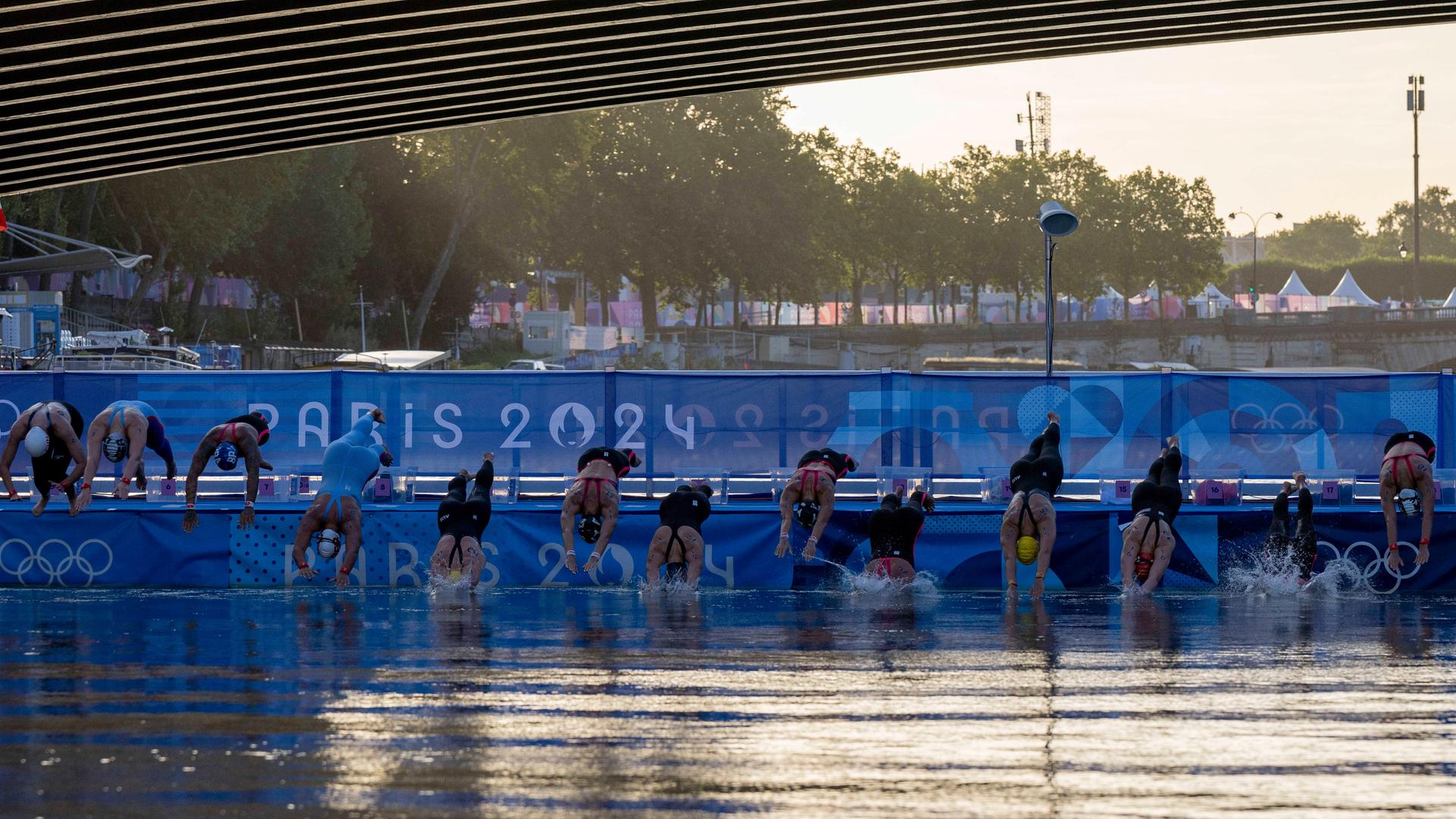 Zu sehen ist der Schwimmstart der Freiwasser-Schwimmerinnen bei den Olympischen Spielen: Eine Reihe von Athletinnen springt mit einem Kopfsprung in die Seine.