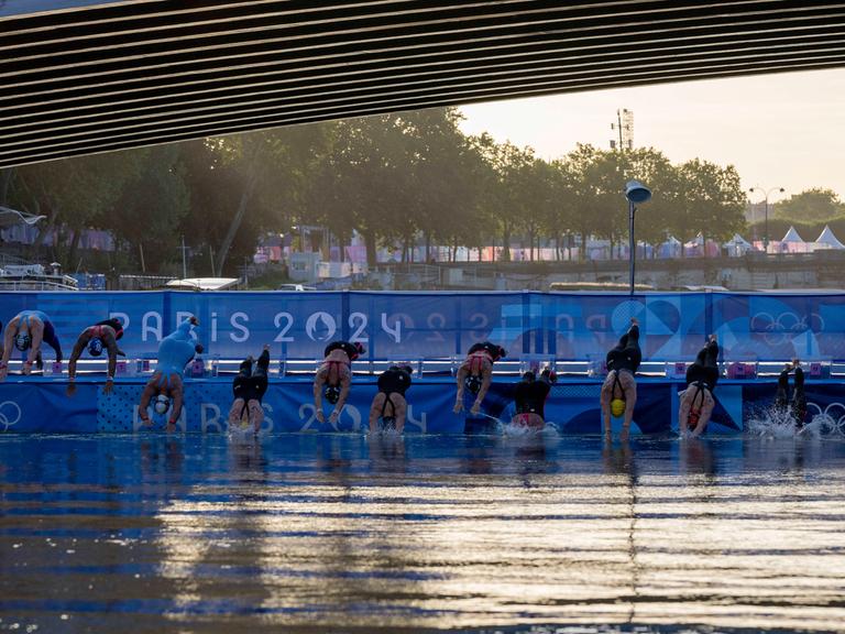 Zu sehen ist der Schwimmstart der Freiwasser-Schwimmerinnen bei den Olympischen Spielen: Eine Reihe von Athletinnen springt mit einem Kopfsprung in die Seine.