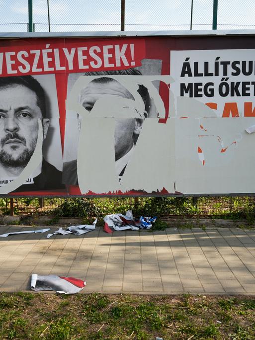 Eine Werbewand in Ungarn während des Wahlkampf. Drei große Plakate waren dort aufgeklebt, doch zwei sind herruntergerissen. Eines ist noch erkennbar. Darauf ist der ukrainische Präsident Selenskij.