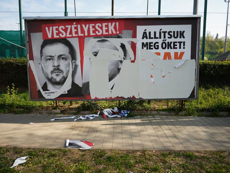 Eine Werbewand in Ungarn während des Wahlkampf. Drei große Plakate waren dort aufgeklebt, doch zwei sind herruntergerissen. Eines ist noch erkennbar. Darauf ist der ukrainische Präsident Selenskij.