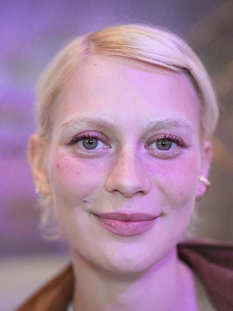 Alli Neumann trägt rosa Lidschatten, steht vor einem violett-rosa beleuchteten Hintergrund und strahlt in die Kamera.