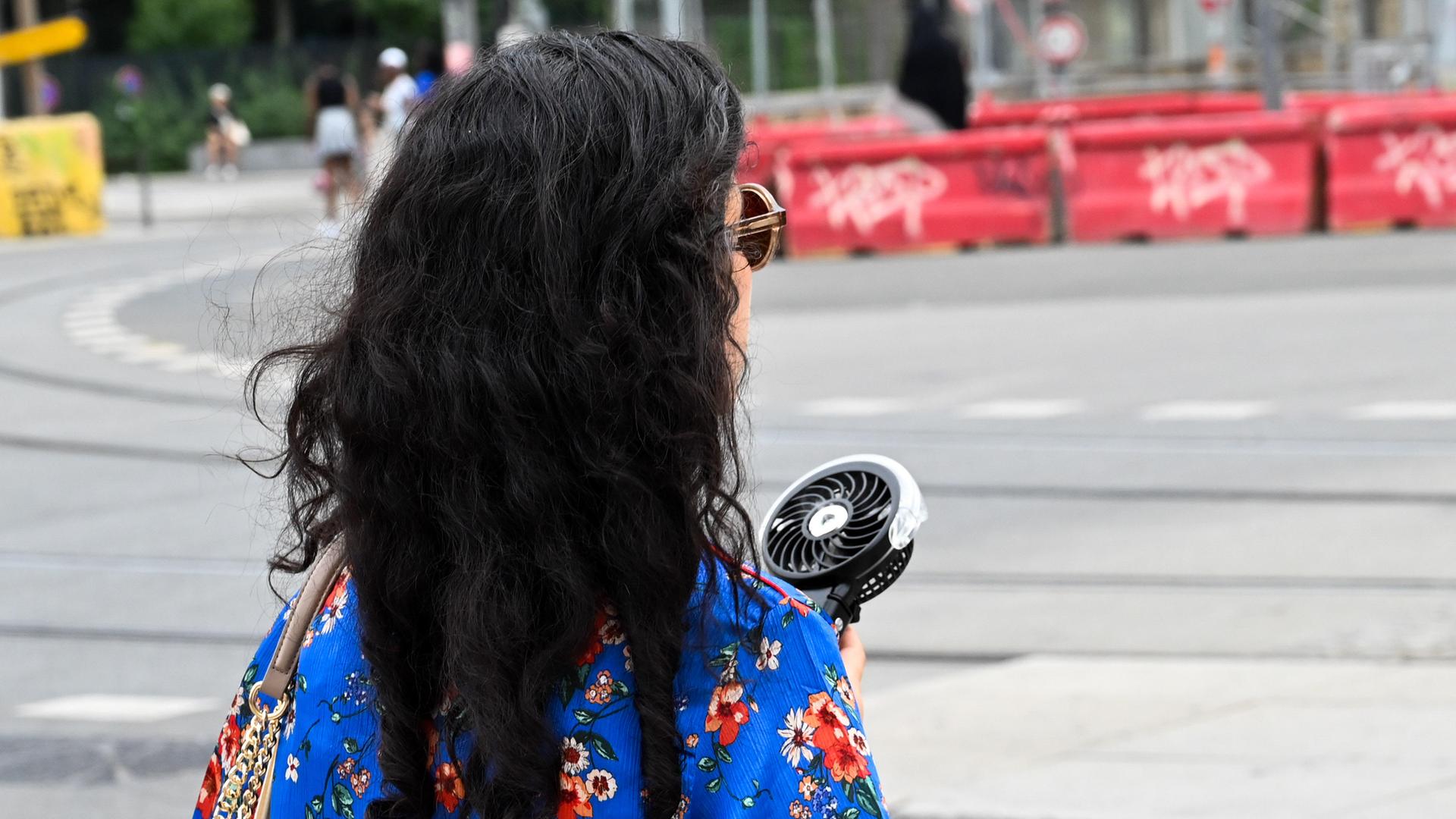 Eine Frau geht in der französischen Stadt Lyon während einer Hitzewelle die Straße entlang. In der Hand hat sie einen kleinen Ventilator, um ihr Gesicht zu erfrischen.