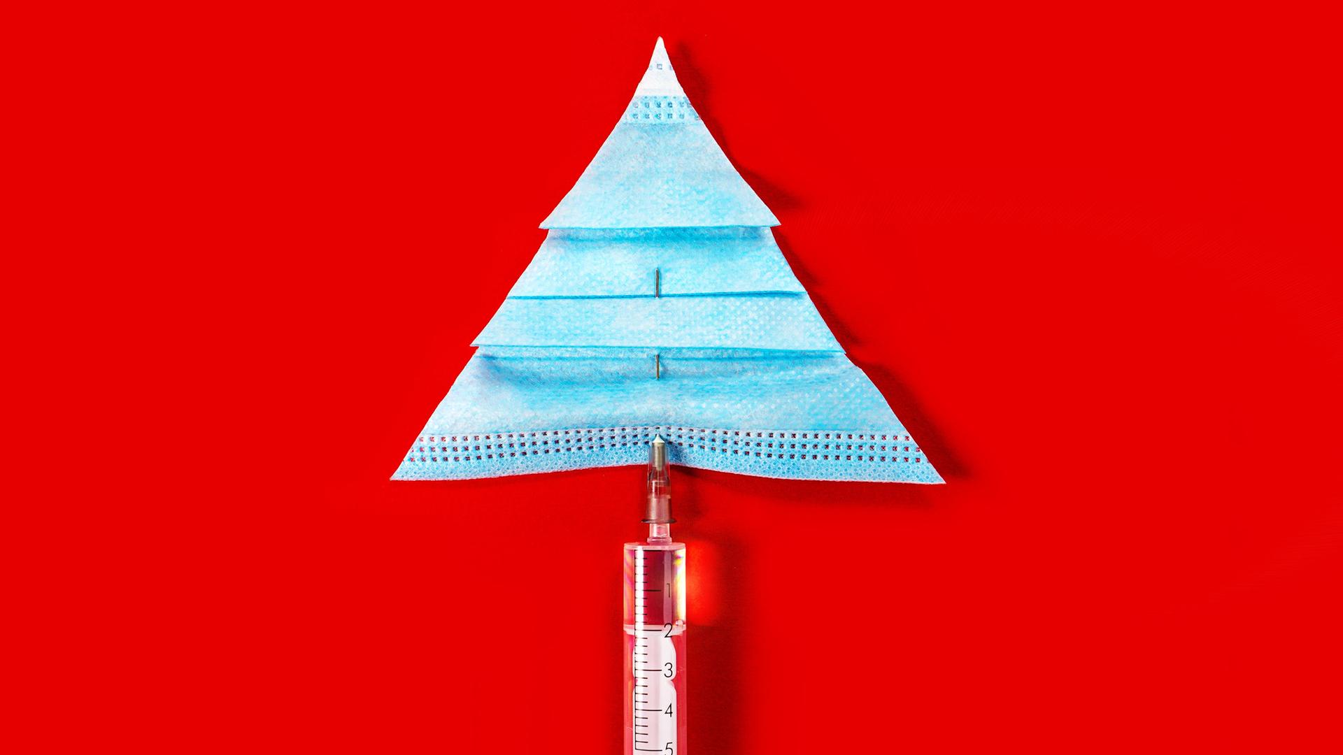 Eine Impfspritze und eine Corona-Maske, die vor rotem Hintergrund einen Tannenbaum bilden.