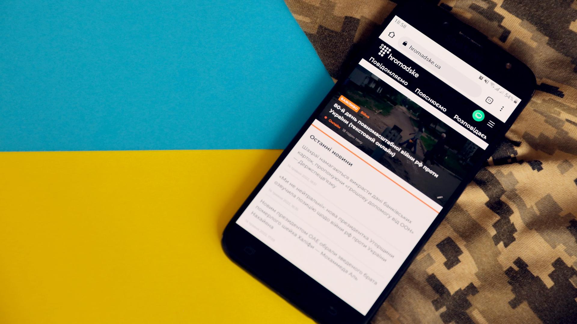Die Homepage des ukrainischen Mediums "Hromadske" auf einem Handybildschirm vor blau-schwarzen und Camouflage-Hintergrund