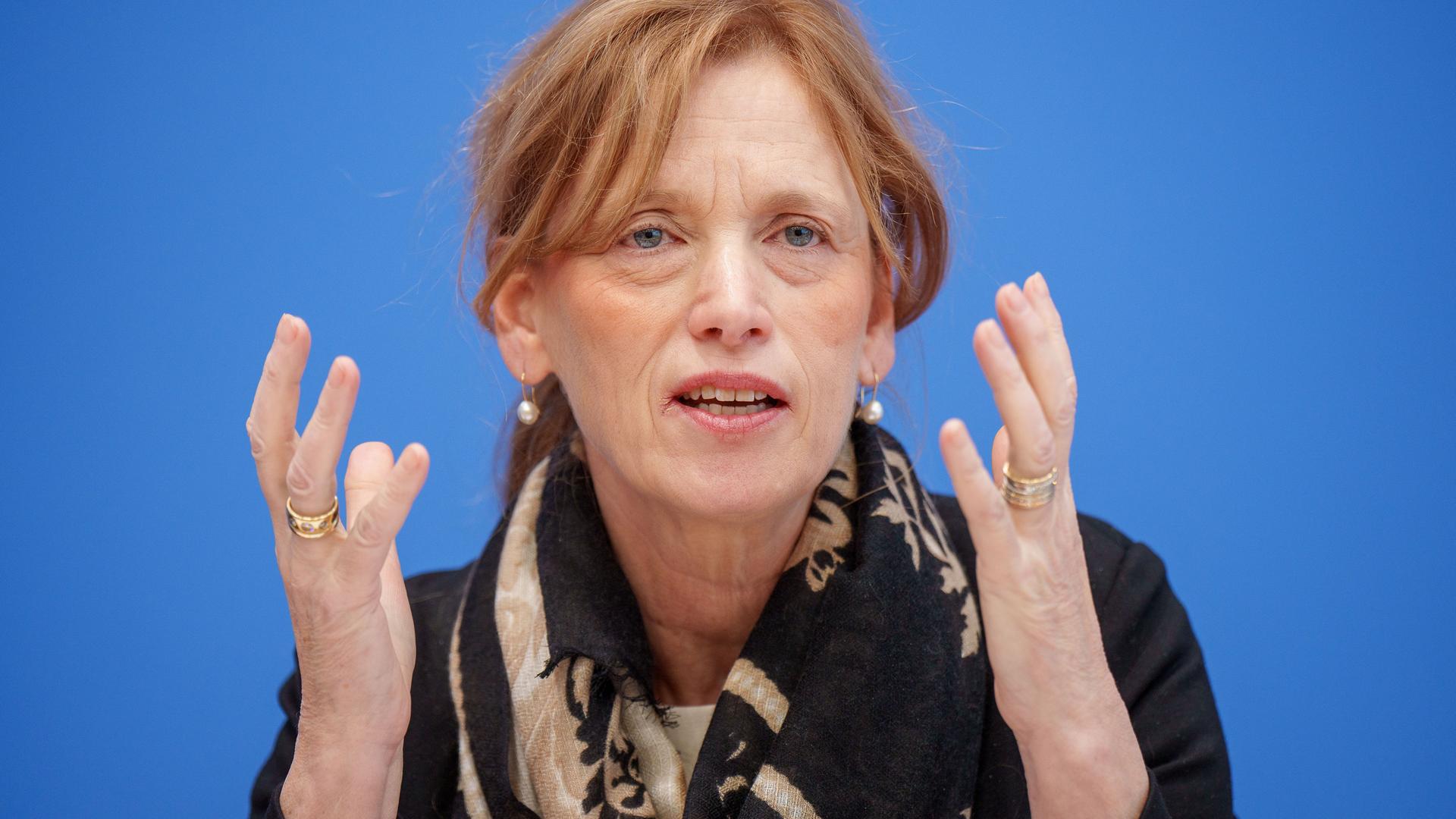 Karin Prien spricht bei einer Pressekonferenz ins Mikrofon und hebt dabei beide Hände.