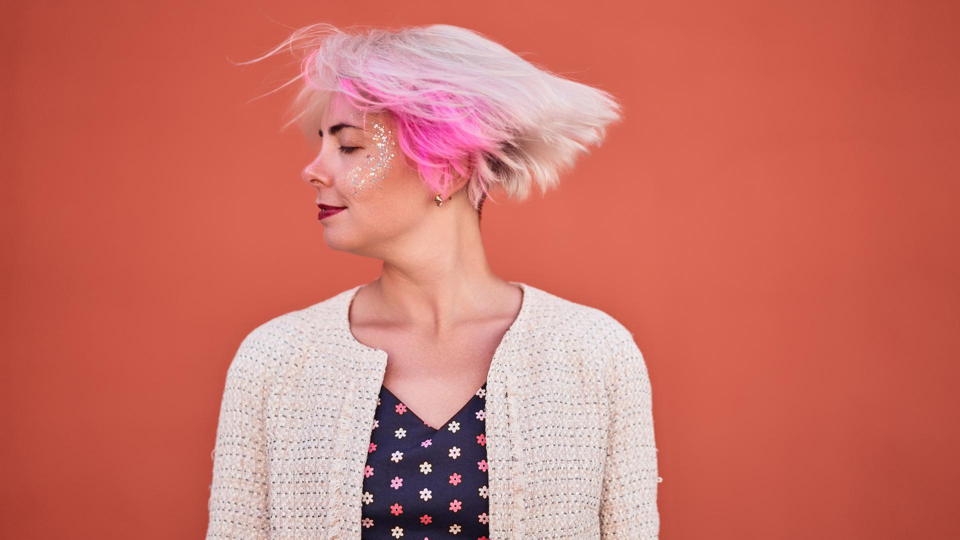 Eine Frau mit blonden Haaren und einer pinken Strähne schüttelt ihren Kopf. 