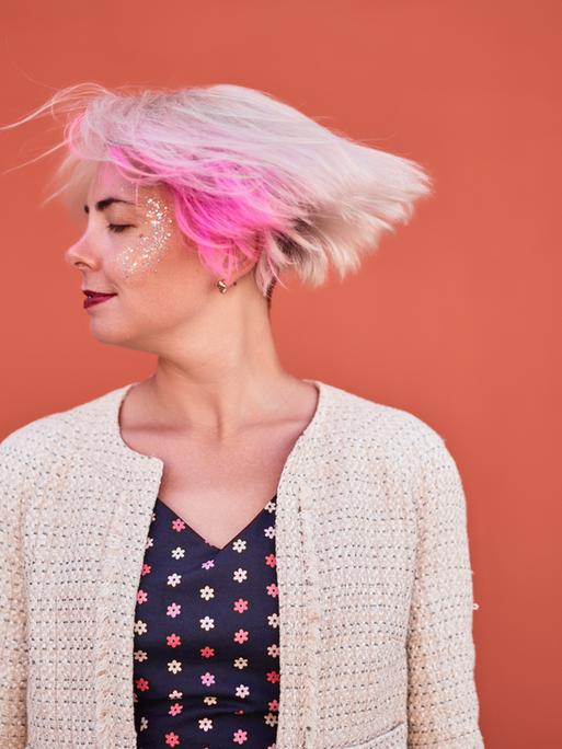 Eine Frau mit blonden Haaren und einer pinken Strähne schüttelt ihren Kopf. 
