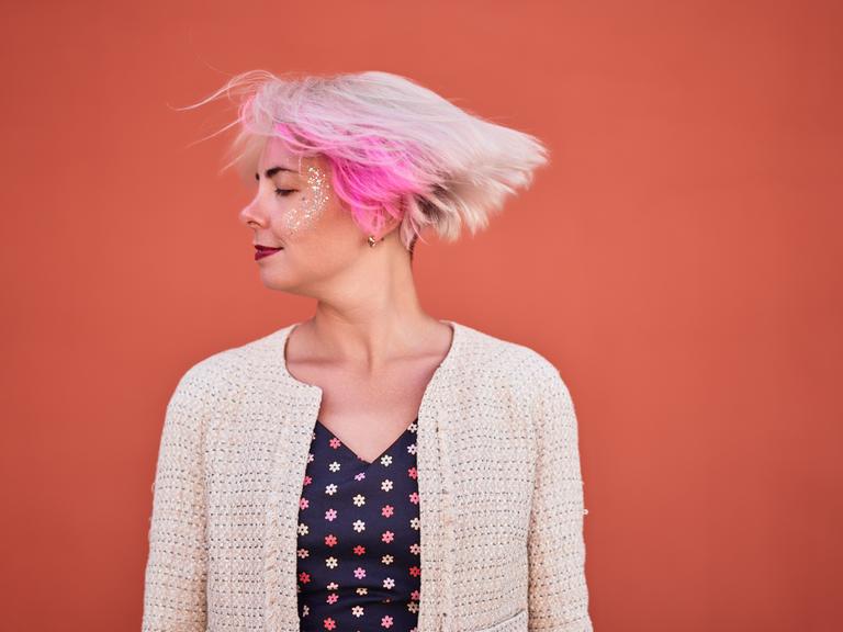 Eine Frau mit blonden Haaren und einer pinken Strähne schüttelt ihren Kopf. 