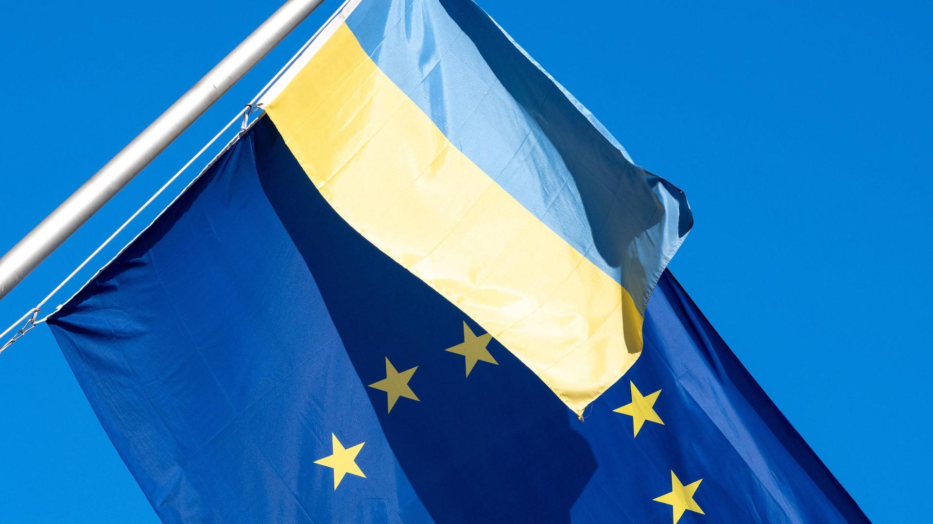 Die EU-Flagge weht zusammen mit einer ukrainischen Flagge vor blauem Himmel.