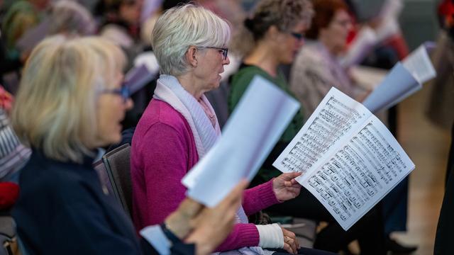 Mehrere Frauen stehen nebeneinander und singen. Sie halten Notenblätter in der Hand.