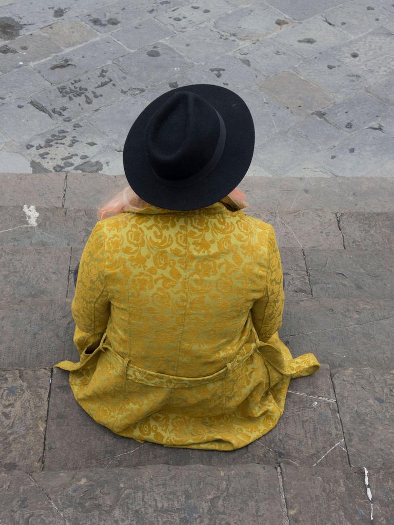 Ein junges Mädchen trägt einen gelben Mantel mit schwarzen Hut und sitzt alleine auf einer Stufe