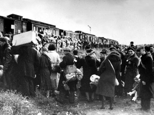 Deportation von niederländischen Juden 1943. Züge warten darauf, sie in ein Konzentrationslager zu bringen. Die Menschen stehen Schlange und haben Koffer, Taschen und viel Gepäck dabei.