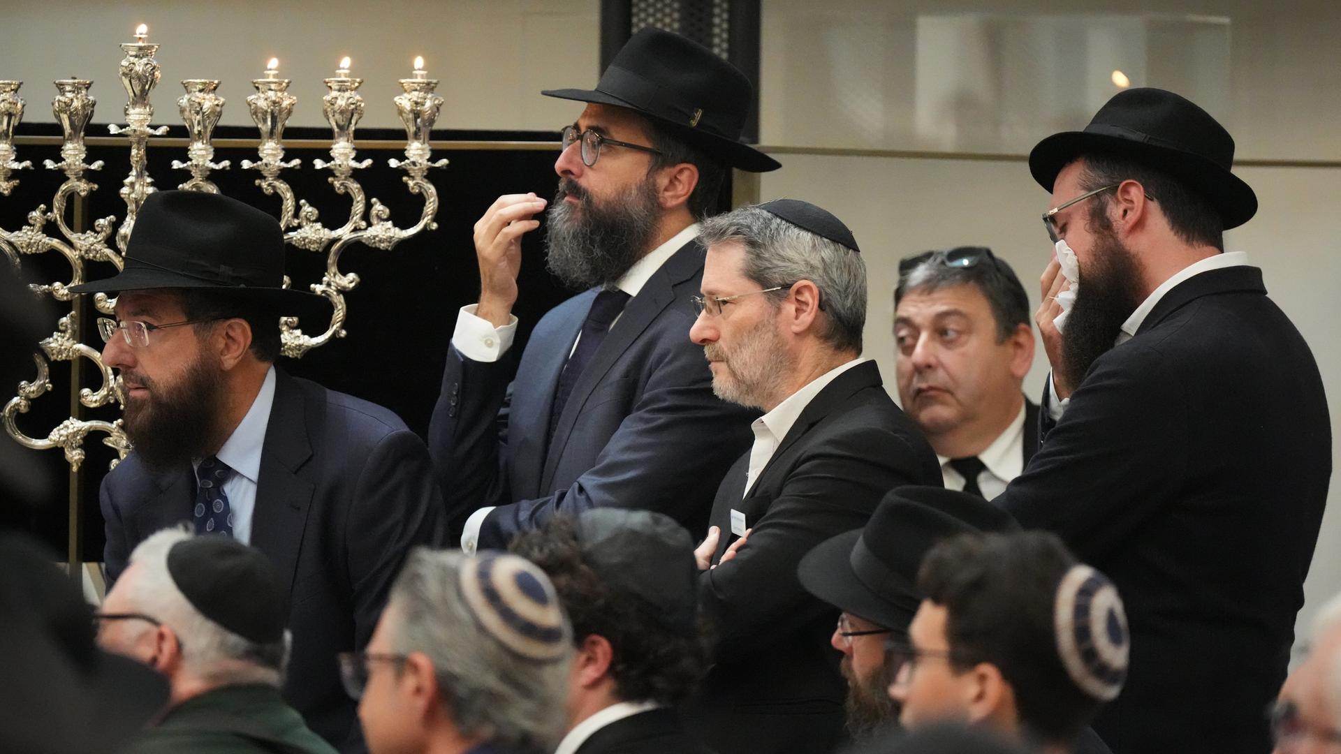 Trauernde jüdische Männer mit Hut oder Kippa in einer Synagoge