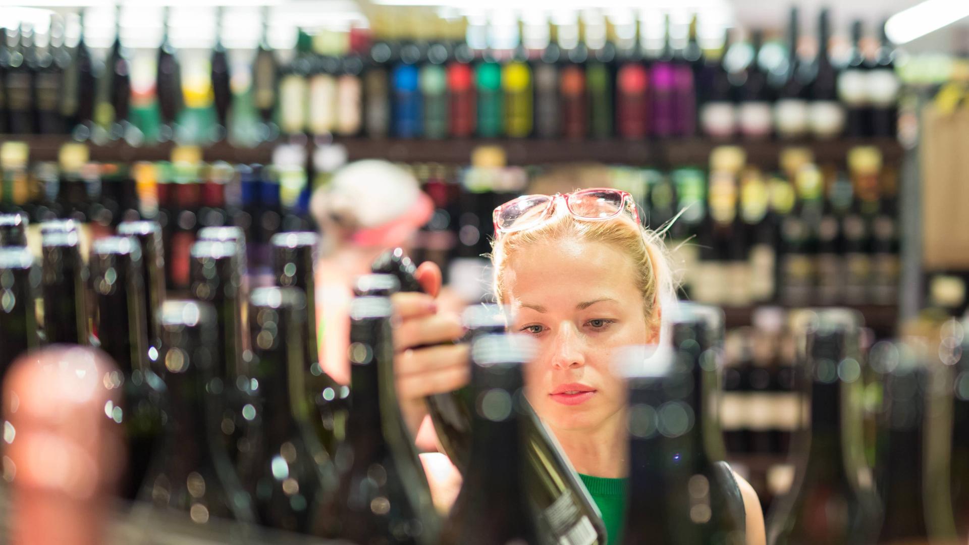 Frau schaut sich im Supermarkt eine Flasche Wein an.