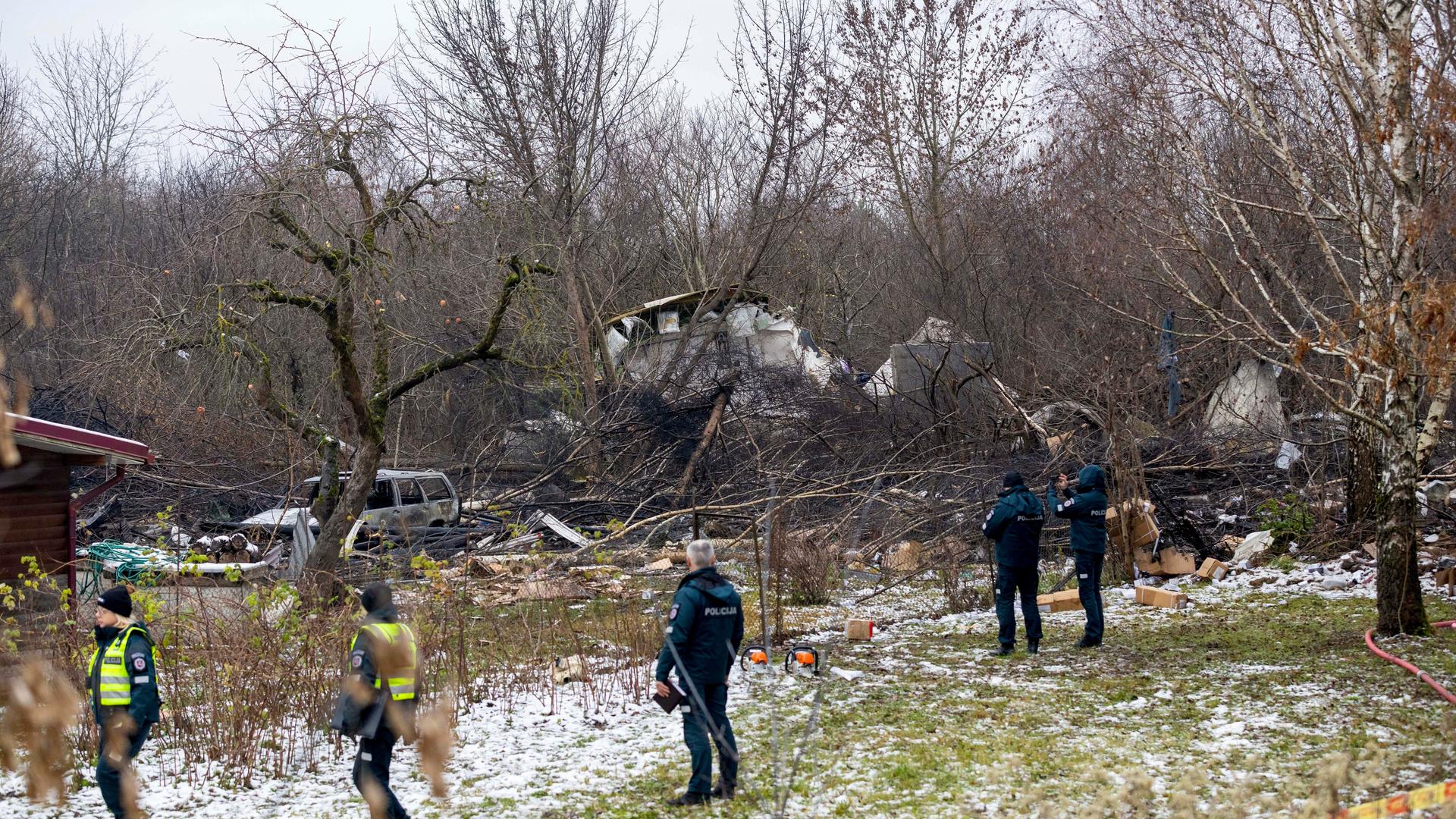 Mitarbeiter des litauischen Katastrophenschutzministeriums und Polizeibeamte stehen in der Nähe der Stelle, an der ein DHL-Frachtflugzeug in ein Haus nahe der litauischen Hauptstadt Vilnius, Litauen, gestürzt ist.