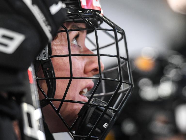 Die deutsche Eishockey-Nationalspielerin Daria Gleißner schaut auf das Spielfeld. Sie trägt einen Helm, ihr Gesicht ist hinter einer Maske geschützt. 