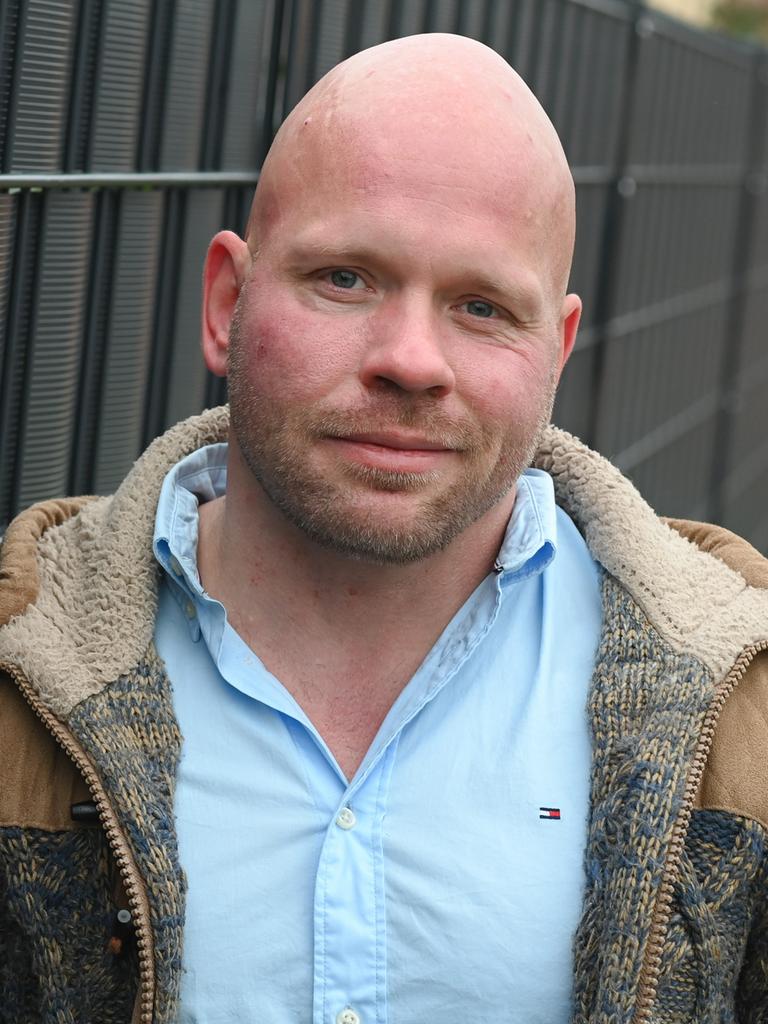 Der Intensivpfleger Ricardo Lange trägt ein hellblaues Hemd und darüber eine offene, braune Jacke und lächelt leicht in die Kamera. Der Intensivpfleger Ricardo Lange trägt ein hellblaues Hemd und darüber eine offene, braune Jacke und lächelt leicht in die Kamera.