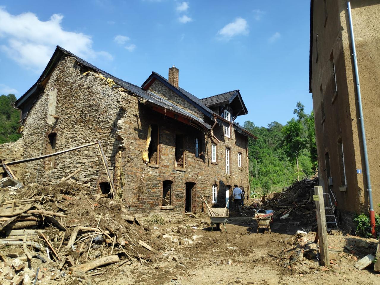 Vor einem alten Backsteinhaus liegen Schutt und Trümmer, eine Menschen und Schubkarren stehen davor.