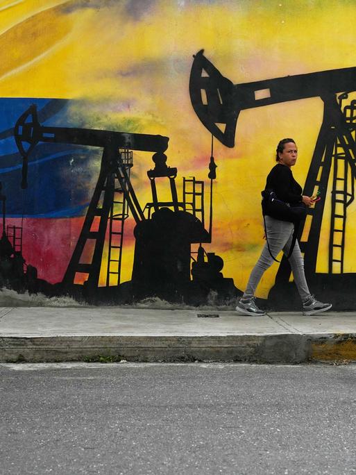 Eine Frau läuft an einem Wandgemälde entlang, das Ölfördertürme auf den Farben der venezolanischen Flagge zeigt.