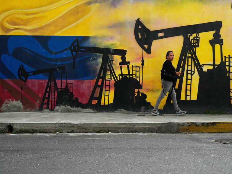 Eine Frau läuft an einem Wandgemälde entlang, das Ölfördertürme auf den Farben der venezolanischen Flagge zeigt.