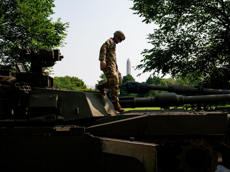 M1 Alpha a3, Abrams Panzer, Stryker und M2 Bradley: Ein US-Soldat steigt über Kampffahrzeuge. Im Hintergrund ist das Washington Monument zu sehen