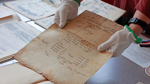 Historische Dokumente werden in einer Ausstellung im Stadtarchiv Halberstadt gezeigt. Eine Person hält ein Dokument hin. Es ist ein altes Papier.
