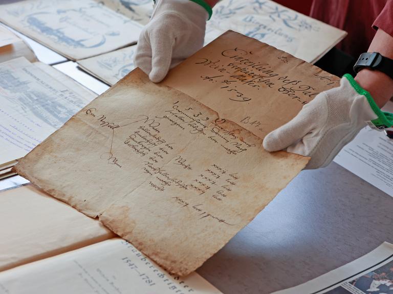 Historische Dokumente werden in einer Ausstellung im Stadtarchiv Halberstadt gezeigt. Eine Person hält ein Dokument hin. Es ist ein altes Papier.