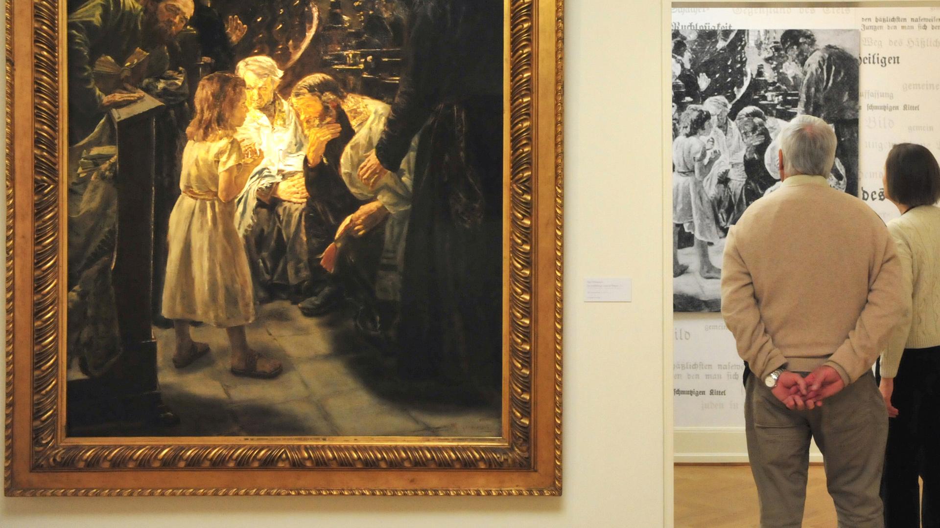 An der Wand links hängt "Der zwölfjährige Jesus im Tempel" von Max Liebermann. Rechts stehen Besucher der Ausstellung, die dem Betrachter den Rücken zuwenden.
