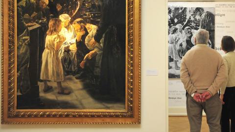 An der Wand links hängt "Der zwölfjährige Jesus im Tempel" von Max Liebermann. Rechts stehen Besucher der Ausstellung, die dem Betrachter den Rücken zuwenden.