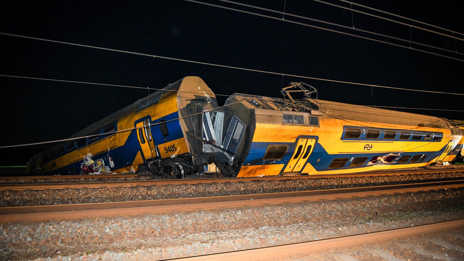 Ein gelb-blauer Zug bei Nacht: Ein Waggon ist entgleist, der Waggon dahinter steht schief auf den Schienen. Ein gelb-blauer Zug bei Nacht: Ein Waggon ist entgleist, der Waggon dahinter steht schief auf den Schienen.
