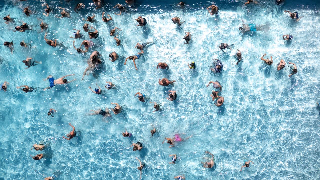Aus Vogelperspektive sieht man zahlreiche Badegäste in einem Wasserbecken eines Freibads schwimmen.