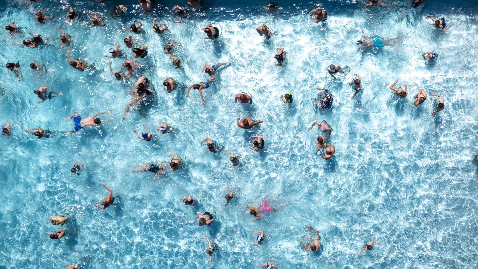 Aus Vogelperspektive sieht man zahlreiche Badegäste in einem Wasserbecken eines Freibads schwimmen.
