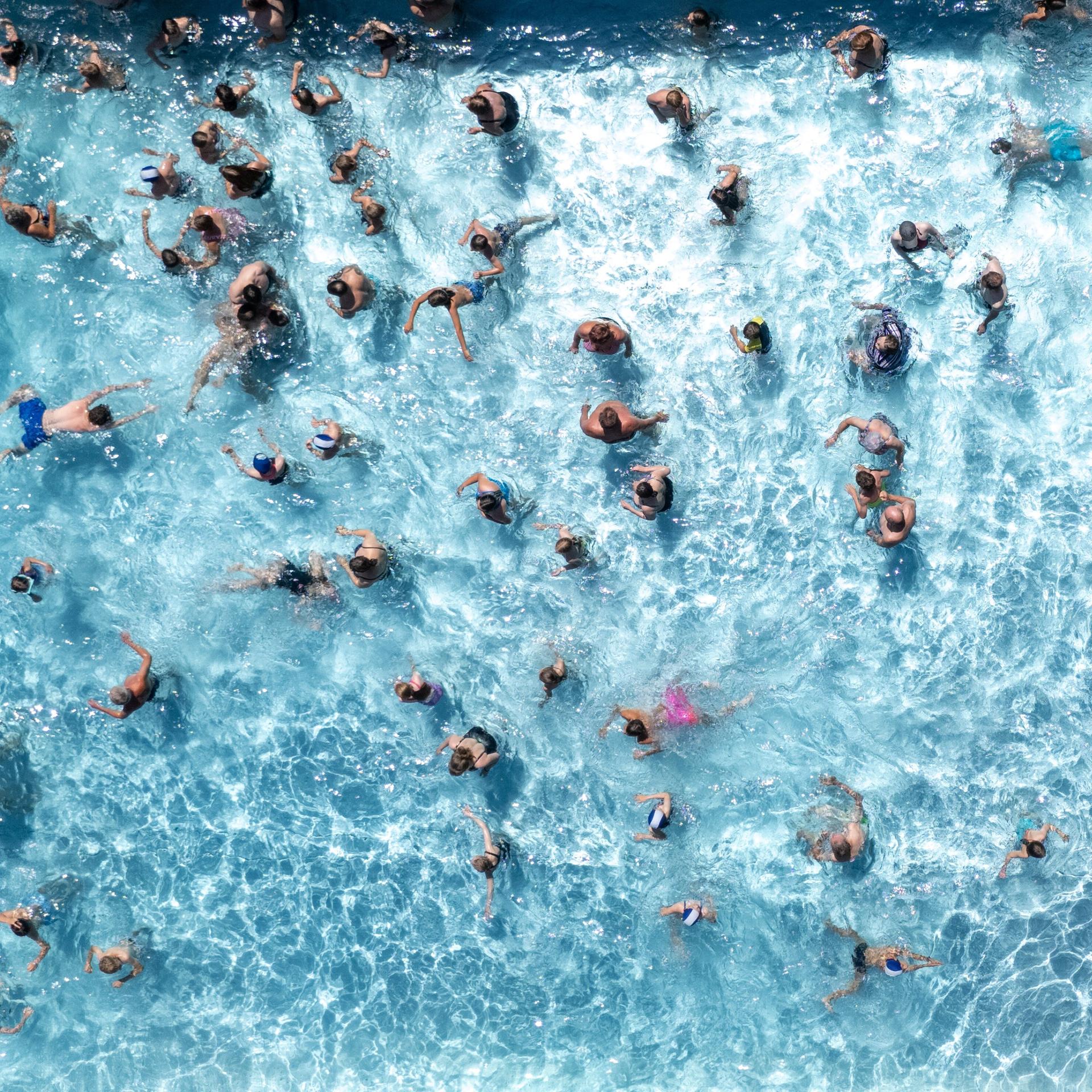 Aus Vogelperspektive sieht man zahlreiche Badegäste in einem Wasserbecken eines Freibads schwimmen.