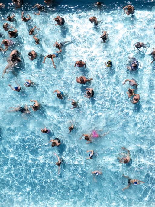 Aus Vogelperspektive sieht man zahlreiche Badegäste in einem Wasserbecken eines Freibads schwimmen.
