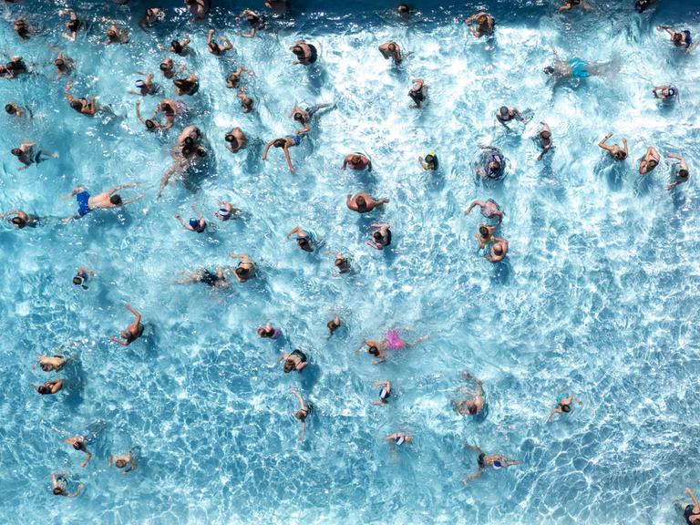 Aus Vogelperspektive sieht man zahlreiche Badegäste in einem Wasserbecken eines Freibads schwimmen.