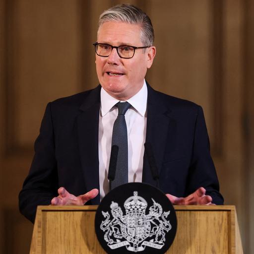 Keir Starmer steht an einem Redner-Pult und spricht. Er trägt einen schwarzen Anzug und eine Krawatte.