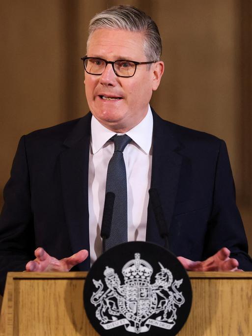 Der britische Regierungschef Keir Starmer steht an einem Redner-Pult und spricht. Er trägt einen schwarzen Anzug und eine Krawatte.