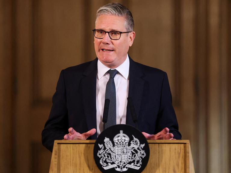 Der britische Regierungschef Keir Starmer steht an einem Redner-Pult und spricht. Er trägt einen schwarzen Anzug und eine Krawatte.