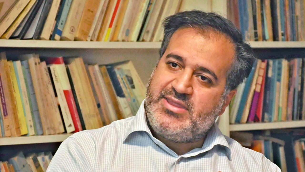 Der Drehbuch-Autor Mehdi Mahmoudian sitz vor einer Bücherwand.