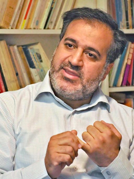 Der Drehbuchautor Mehdi Mahmoudian sitz vor einer Bücherwand. Er zählt Argumente an seinen Fingern ab