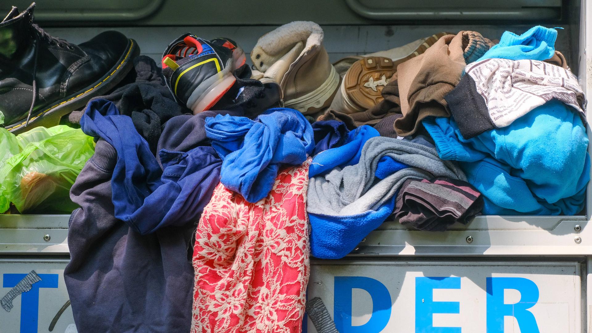 Kleidungsstücke und Schuhe liegen auf einem übervollen Altkleidercontainer.