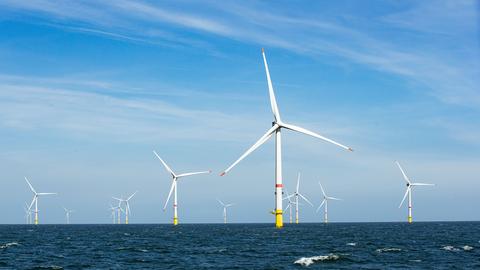 Windräder stehen vor blauem Himmel auf dem offenen Meer.