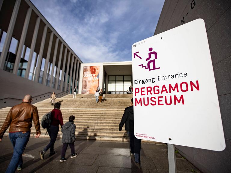 Menschen gehen die Treppe zur James Simon Galerie auf der Berliner Museumsinsel hinauf. Auf einem Schild rechts steht: Eingang Pergamonmuseum. 