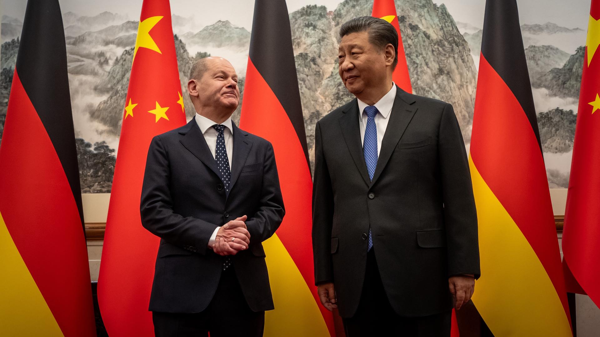 Das Foto zeigt Bundeskanzler Scholz und den chinesischen Präsidenten Xi Jingping. Im Hintergrund sind deutsche und chinesische Flaggen. 