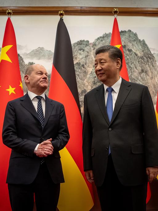 Bundeskanzler Scholz (mit ineinander gelegten Händen) und der chinesische Staatspräsident Xi Jinping posieren vor den Flaggen Deutschlands und Chinas.