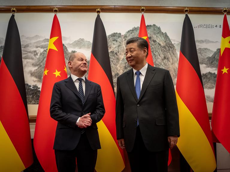 Bundeskanzler Scholz (mit ineinander gelegten Händen) und der chinesische Staatspräsident Xi Jinping posieren vor den Flaggen Deutschlands und Chinas.